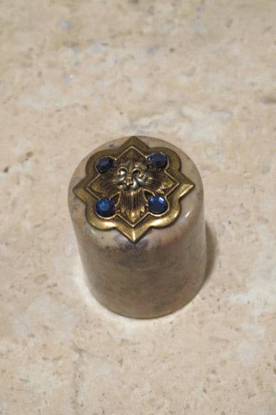 Jo Marz jeweled fleur de lis trinket box with brass finish and blue gem accents on a beige stone surface