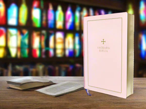 Pink Catholic Bible for gifts with gold cross and title Sagrada Biblia on wooden table in church