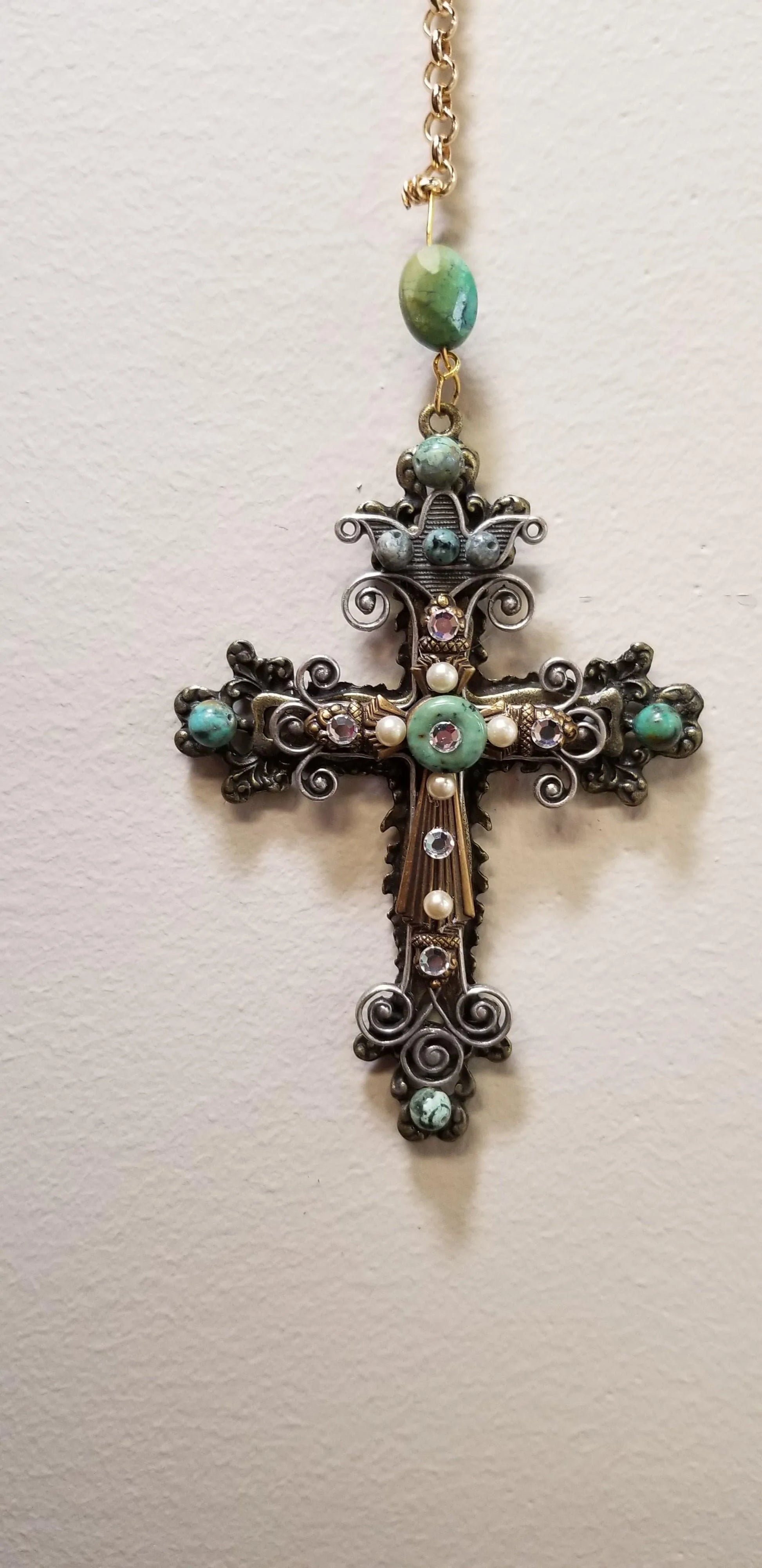 Dacole Designs jeweled cross ornament with turquoise stones and intricate metal scrollwork hanging on wall