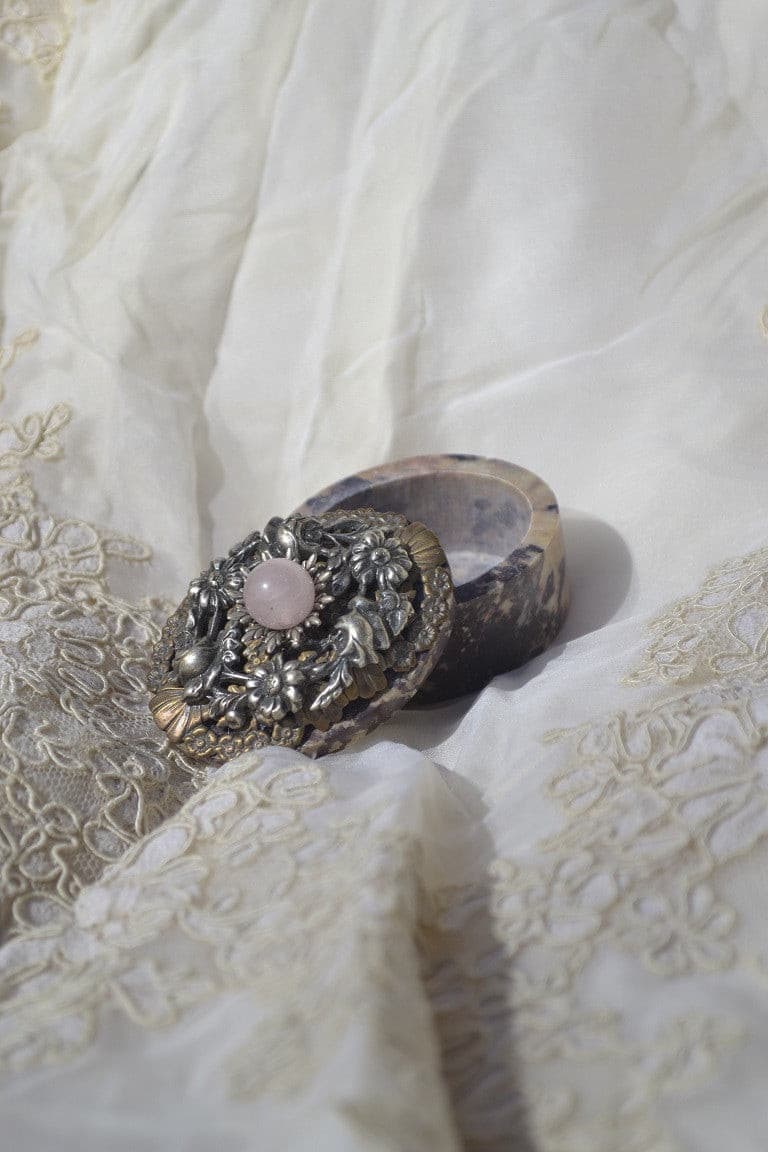 DeMartineau jeweled soapstone keepsake box with ornate floral lid and pink stone accent on fabric