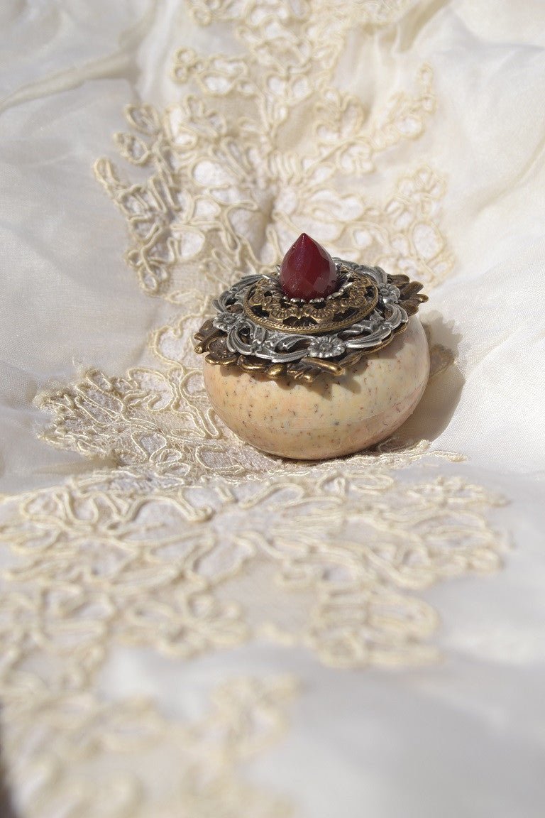 Dacole Designs jeweled soapstone keepsake box with ornate metal lid and red gemstone on cream lace fabric