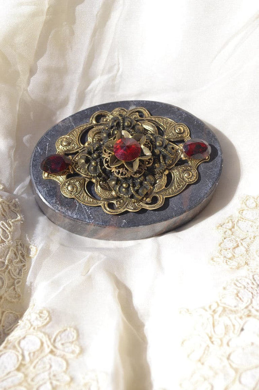 DeMartineau jeweled soapstone paperweight with ornate gold filigree and red gemstones on white fabric